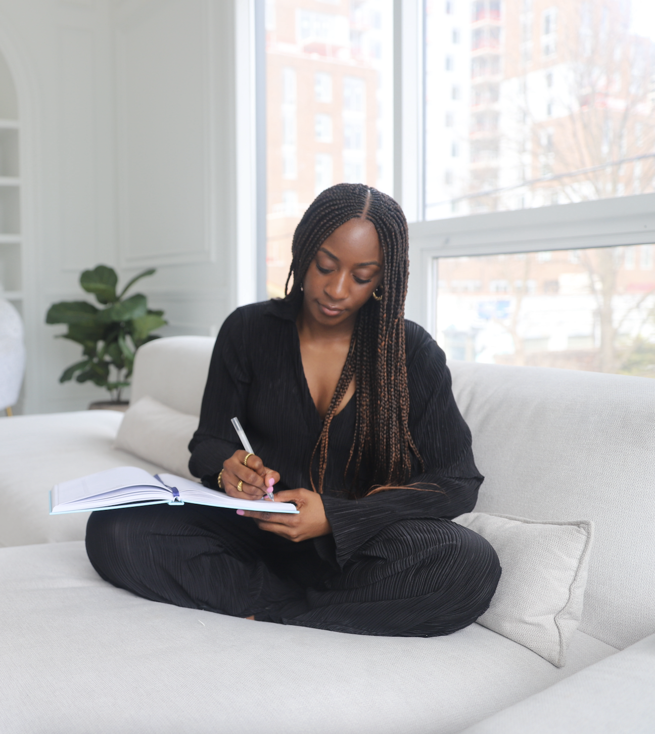 Girl sitting on a couch wearing black and writing in a journal